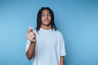 Genç bir birey, parmaklarının arasında küçük pembe bir nesne tutarak güvenle ayakta duruyor. Arka plan canlı bir mavi, canlı atmosferi arttırıyor. Gündelik beyaz giysi rahatlatıcı bir hava katıyor..