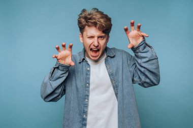 Kot gömlek ve beyaz tişört giyen genç bir adam oyuncu ama vahşi bir ifade sergiliyor. Yumuşak mavi bir arka plana karşı poz veriyor, enerji ve eğlenceyi somutlaştırıyor..