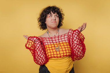 Bir model belirsiz bir ifadeyle ayakta duruyor, kırmızı ağ ile kaplanmış sarı bir üst katman sergiliyor. Parlak sarı arka plan kıyafetin neşeli havasını arttırır..