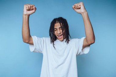 Genç bir insan mutluluğunu kaldırılmış yumruklar ve kocaman bir gülümsemeyle ifade eder. Şahıs, mavi bir arkaplana karşı kaygısız bir an sergiliyor..