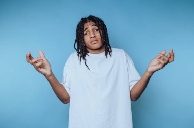 Genç bir adam omuz silkerek, belirsizlik ve kafa karışıklığı içinde duruyor..