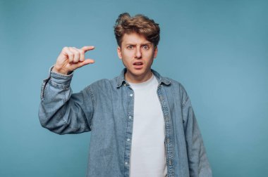 Kot ceketli genç bir adam parmaklarıyla hareket ederken şaşkınlığını gösterir. Bu da bir şeyin çok küçük olduğunu gösterir. Arkaplan, sıradan atmosfere eklenen bir mavidir..