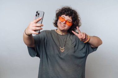 Genç bir birey, bir elinde akıllı bir telefon, diğer elinde barış işareti tutarak güvenle ayakta duruyor..