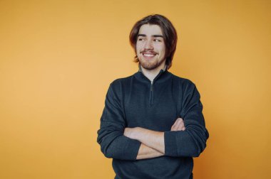 Genç bir adam kolları bağlıyken gülümser ve kendinden emin bir tavır sergiler. Canlı turuncu arka plan onun etrafındaki canlı atmosferi güçlendiriyor..