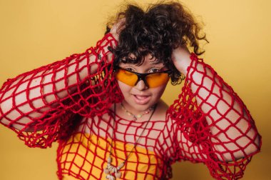 Bir model, sarı bir kıyafetin üzerine kırmızı ağlı bir bluz giyerek neşeli bir enerjiyle poz verir. Çarpıcı renkler ve gevşek titreşim yaratıcı moda ifadesini vurguluyor.