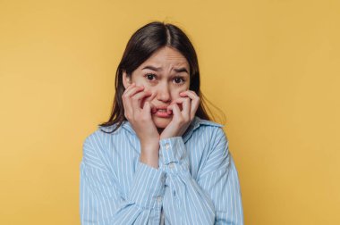 Elleri yüzünü kavrayan ve endişeli bir ifadeyle genç bir kadın gözle görülür şekilde endişeli görünüyor. Parlak sarı arka plan duygularının yoğunluğunu arttırıyor..