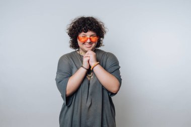 Kıvırcık saçlı, kendine güvenen, gülümseyen, turuncu güneş gözlüklü ve bol gri gömlekli biri. Birbirlerine tutunuyorlar, neşeli bir hava yayıyorlar..