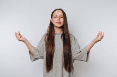 Uzun saçlı genç bir kadın farkındalık meditasyonu uyguluyor, elleri mudra pozisyonunda, gözleri kapalı, hafif ışıklandırılmış bir mekanda sükunet ve sükunet yayıyor..