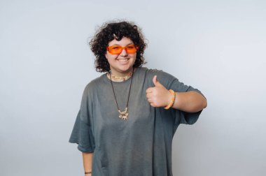 Turuncu güneş gözlüğü takan kıvırcık saçlı bir insan onay verir..