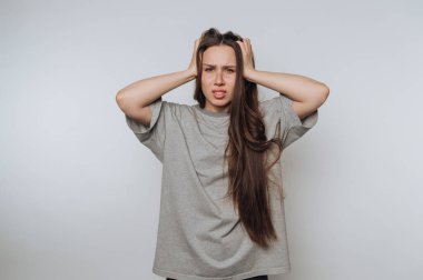 Uzun saçlı genç bir kadın stresli görünüyor, iki elini de arka planda tutuyor..