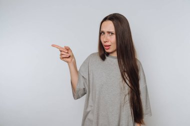 Gri tişörtlü, uzun saçlı bir kadın şaşırmış bir ifadeyle yan tarafı işaret ediyor..
