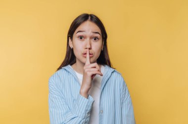 Genç bir kadın sarı arka plana karşı sessiz bir jest yapıyor..