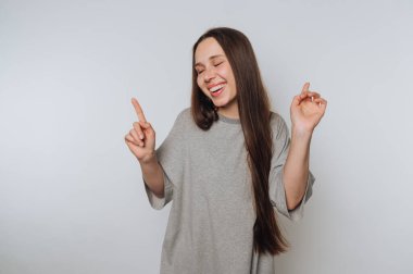 Gri bir gömlekle arka planda dans eden uzun saçlı neşeli bir genç kadın..