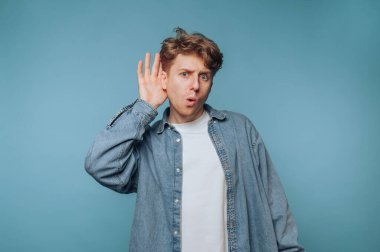 Şaşırmış bir ifadeyle genç bir adam elini kulağına dayayıp dikkatle dinliyor..