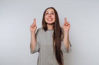 Uzun saçlı bir kadın parmaklarını çapraz yapıp gülümsüyor, umut dolu görünüyor..