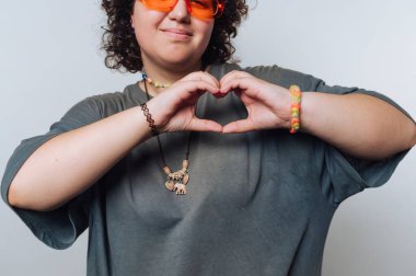 Turuncu güneş gözlüğü takan insan elleriyle kalp şekli yapar..