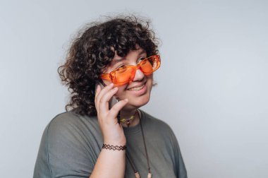 Turuncu güneş gözlüğü takan kıvırcık saçlı biri telefonla konuşuyor, gülümsüyor..