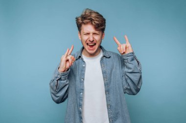 Kot gömlekli genç adam mavi arka planda rock 'n roll hareketi yapıyor..