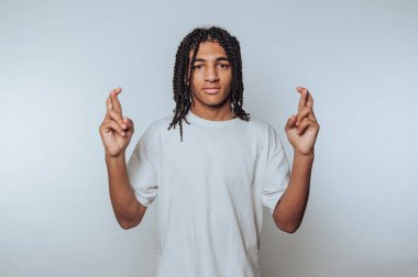 Sade bir arka planda beyaz tişört giyen örgülü saçları olan genç bir adam..