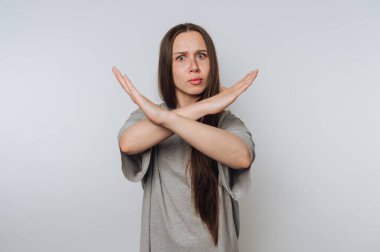 Uzun saçlı bir kadın kollarıyla X hareketi yapıyor, gri bir gömlek giyiyor..