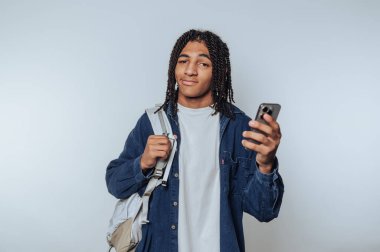 Saçları örgülü, akıllı bir telefon tutan ve sırt çantası takan genç bir adam, özgüvenli ve sıradan bir tavır sergiliyor..