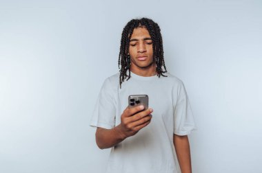 Saçı örgülü genç adam arka planda akıllı telefona bakıyor..
