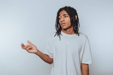 Saçları örgülü, beyaz tişörtlü, elleri arka planda olan genç bir adam..