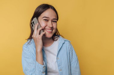 Gülümseyen genç bir kadın sarı arka planda akıllı bir telefonla konuşuyor..