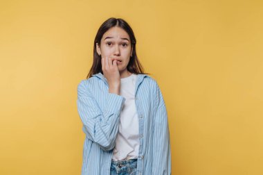 Tırnaklarını sarı arka planda yiyen endişeli bir yüzü olan genç kadın..