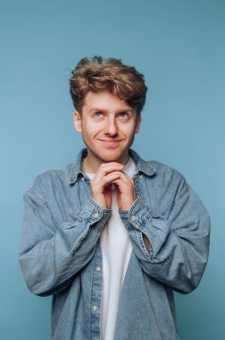 Neşeli bir yüzü olan genç bir adam, mavi arka planda kot gömlek giyiyor..