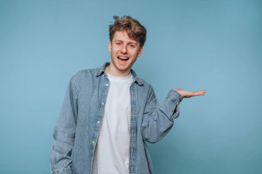 Kot gömlekli genç adam mavi arka planda el kol hareketi yapıyor..