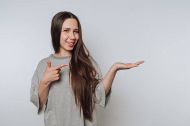 Gri gömlekli, uzun saçlı genç bir kadın elini işaret ediyor..