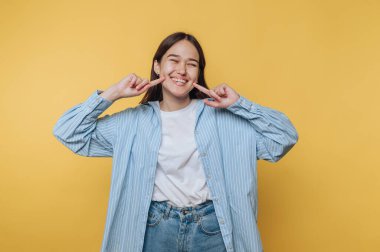 Gülümseyen ve yanaklarını sarı arka plana gösteren genç bir kadın..