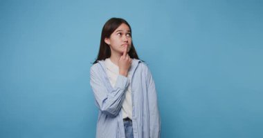 Genç bir kadının parlak mavi bir arka plana karşı düşünceli bir şekilde duruşu.