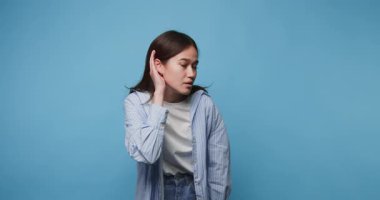 Mavi arka planda dikkatle dinleyen genç bir kadın merak ve nişanı gösteriyor.