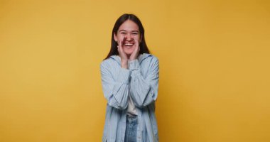 Parlak gülüşlü neşeli kadın canlı sarı bir arkaplan karşısında heyecanını ifade ediyor.