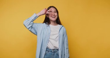 Stüdyo ortamında canlı sarı bir arka plana gülümseyen ve şakacı poz veren genç bir kadın.