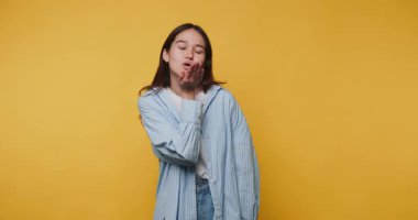 Güzel Asyalı kız yüzünde bir gülümsemeyle kameraya kur yapıyor, bir öpücük yolluyor ve sarı arka planda bir kalp gösteriyor.