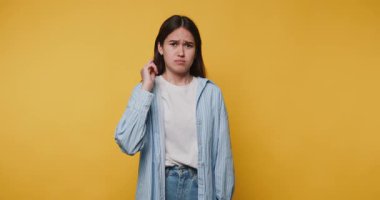 Parlak sarı arka planda kafa karışıklığı gösteren genç bir kız. Duygularını ve vücut dilini kameraya doğru gösteren hoş olmayan bir işaret.