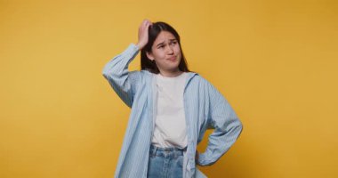 Genç bir kadın, günlük kıyafet giyerken parlak sarı bir arka plan karşısında şaşkın görünüyor.