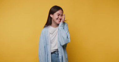 Genç bir kadın güler ve yüzünü canlı sarı bir zemine bastırır neşeli bir anda