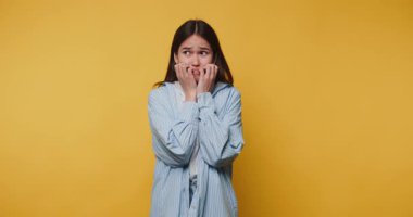 Gergin genç kadın, parlak sarı arka plan önünde kaygısını dile getiriyor.