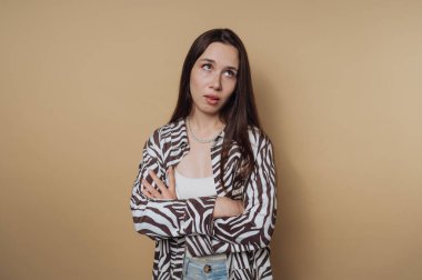 Kollarını kavuştururken gözlerini deviren genç bir kadın portresi, sakin sarı arka planda rahatsız edici ya da iğneleyici bir tavır sergiliyor.