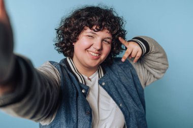 Mavi arka planda selfie çekerken neşeli genç bir kadının portresi.