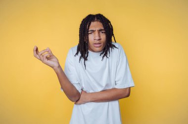 Şaşkın bir ifadeyle genç bir adamın portresi sarı arka planda kafa karışıklığını gösteren kollarını çapraz tutuyor.