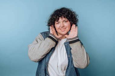 Genç bir kadının portresi dinliyormuş gibi gülümsüyor, mavi arka planda neşeli ve neşeli bir kişilik sergiliyor.