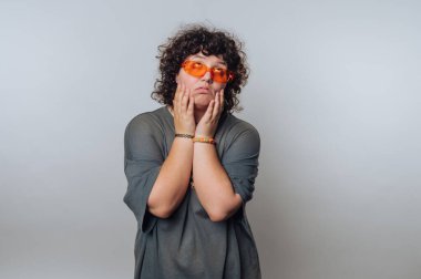 Şaşırmış kıvırcık saçlı genç kadının portresi, açık arkaplanda neşeli ama endişeli bir ifade sergilerken merak ve düşünceli bir görünüm sergiliyor.