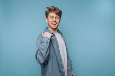 Gencin portresi, açık mavi arkaplanda pozitiflik ve dostluk saçan geniş bir gülümsemeyle başparmak kaldırıyor.