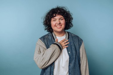 Genç bir kadının portresi göğsüne sıcacık bir gülümsemeyle dokunuyor. Mavi arka planda bir sıcaklık ve takdir hissi veriyor.