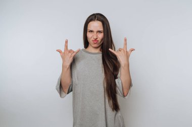 Genç bir kızın portresi elleriyle bir kaya işareti yapıyor, açık arkaplanda neşeli tavrını sergiliyor.